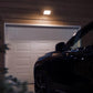 Car parked in front of a white garage door at night with a light fixture above.